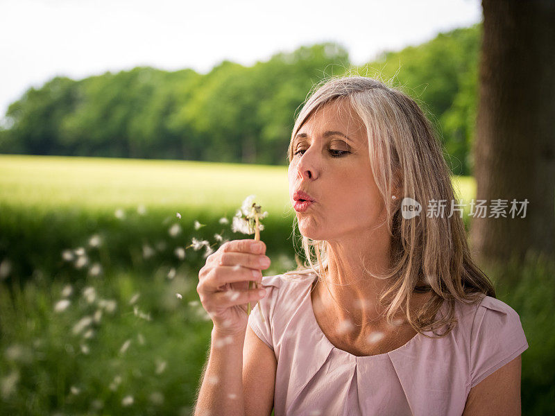 成熟的女人从自然界吹出蒲公英的种子