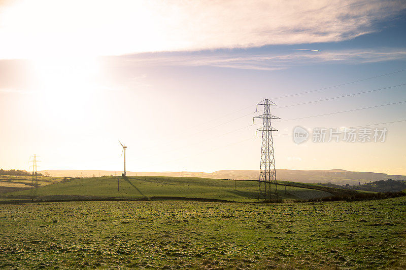 阳光照耀在朦胧的田野与塔和风力涡轮机
