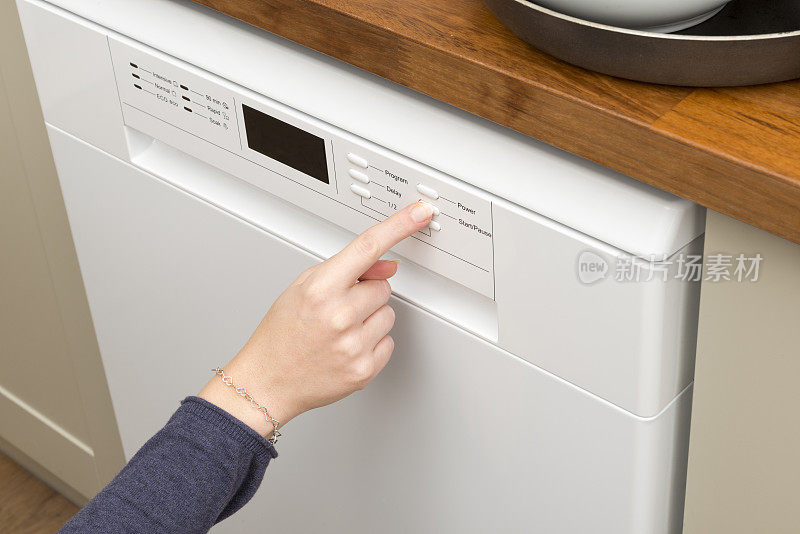 女人的手指按下洗碗机的启动按钮