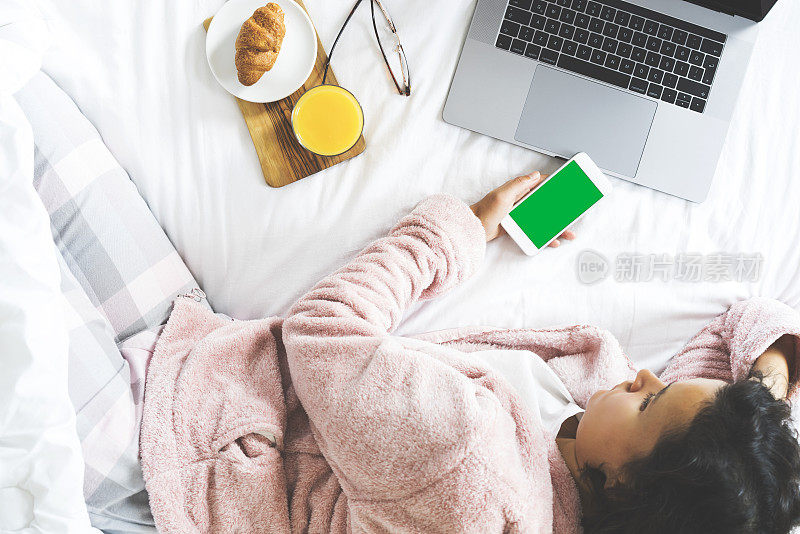 年轻女子躺在床上用绿屏智能手机