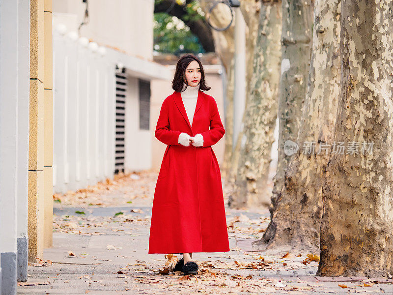在秋天的城市里，穿着红色外套的漂亮年轻女子。户外时尚写真魅力年轻的中国开朗时尚女士在街头。情感、人、美、生活理念。
