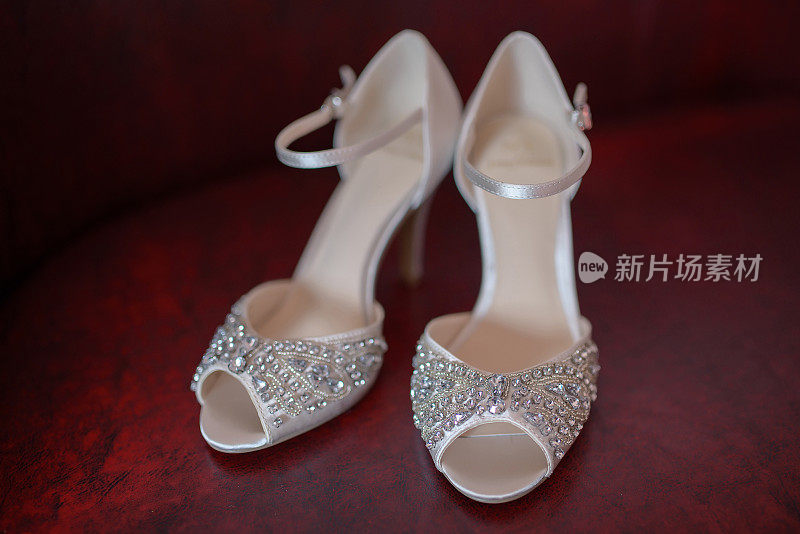 白色丝质新娘露趾鞋与莱茵石和精致的珠子，充分显示，在一对，在一个深红色的背景