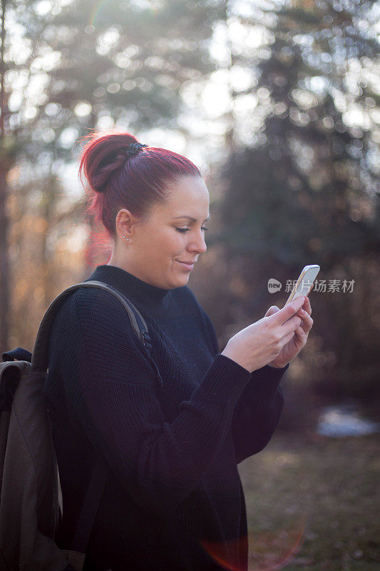 微笑的年轻女子在看她的智能手机户外照片上的信息