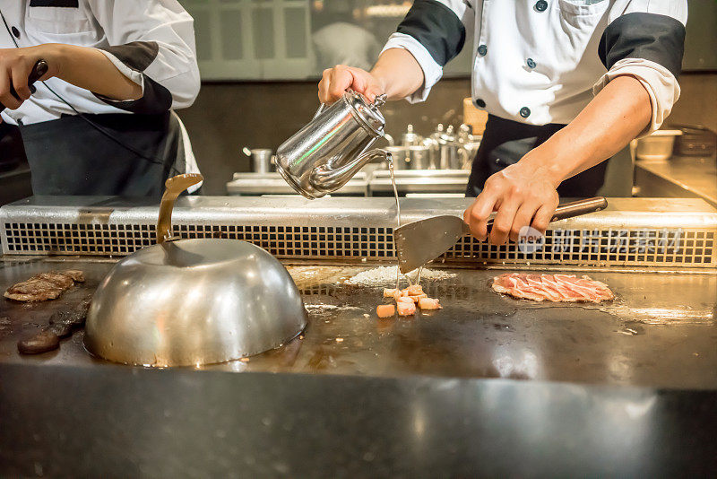 厨师的手在顾客面前将水倒入热锅中。日本Tepanyaki牛排