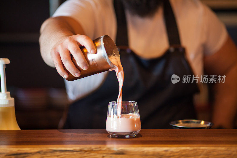 调酒师将一杯新鲜的酒精鸡尾酒倒入玻璃杯