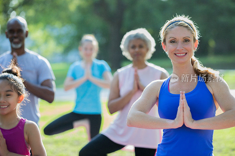 中年女性教授户外瑜伽课程给不同的学生