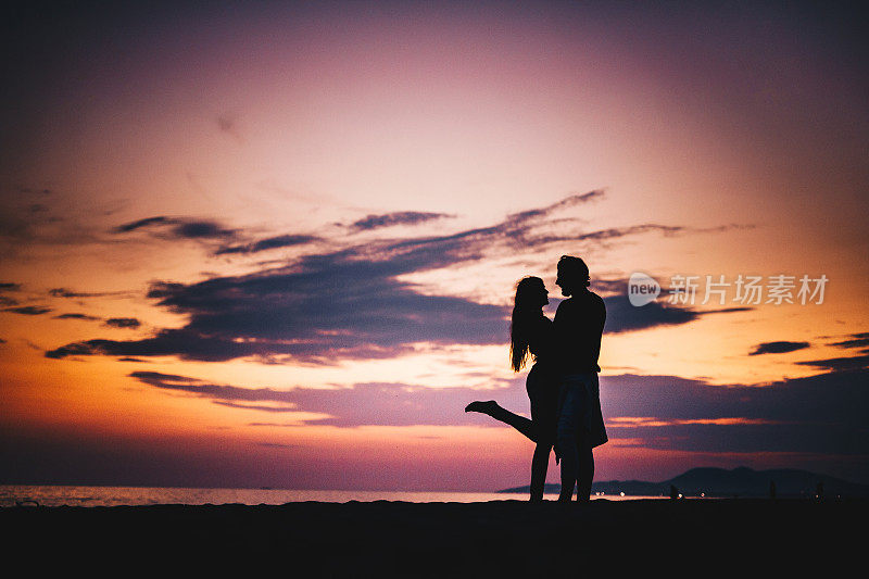 日落时分沙滩上一对浪漫情侣的剪影。