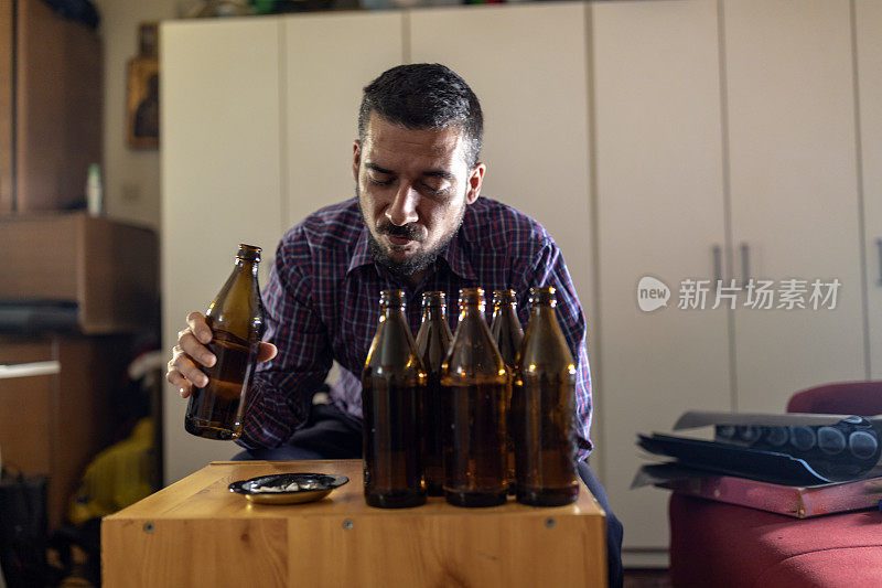 年轻悲伤的醉酒男子喝啤酒和酒精感到浪费，孤独和绝望的痛苦和情绪压力。人与酗酒、上瘾和男人抑郁的概念。