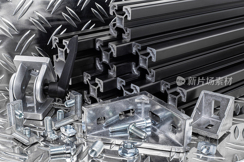 堆叠黑色阳极氧化铝挤压棒，连接器，接头，螺丝，槽螺母和角支架银色闪亮的钻石板背景。建筑金属钢厂概念。