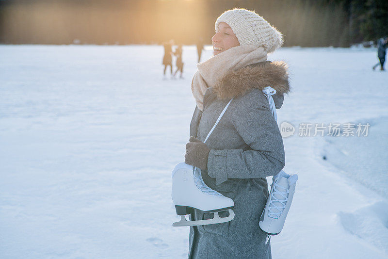 夕阳西下，年轻女子肩挎冰鞋走在结冰的湖面上，享受着寒假的乐趣