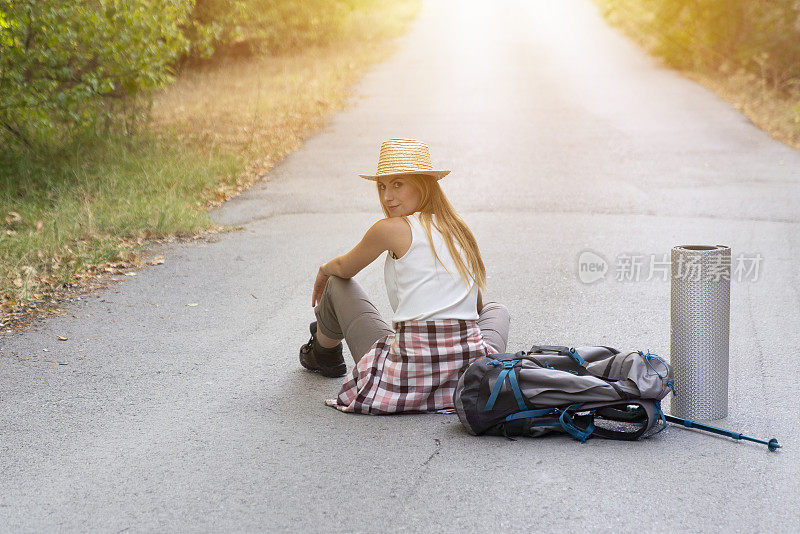 女旅人坐在路上，望着别处的路。背包徒步者在路上放松，欣赏日落