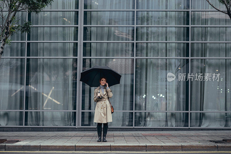 一个拿着雨伞的女人站在街上打手机