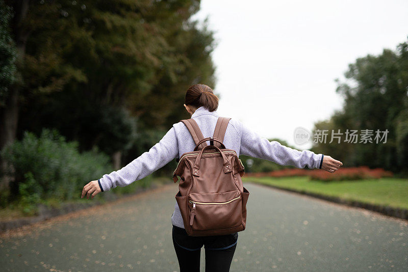 女人在秋天公园散步的后视图