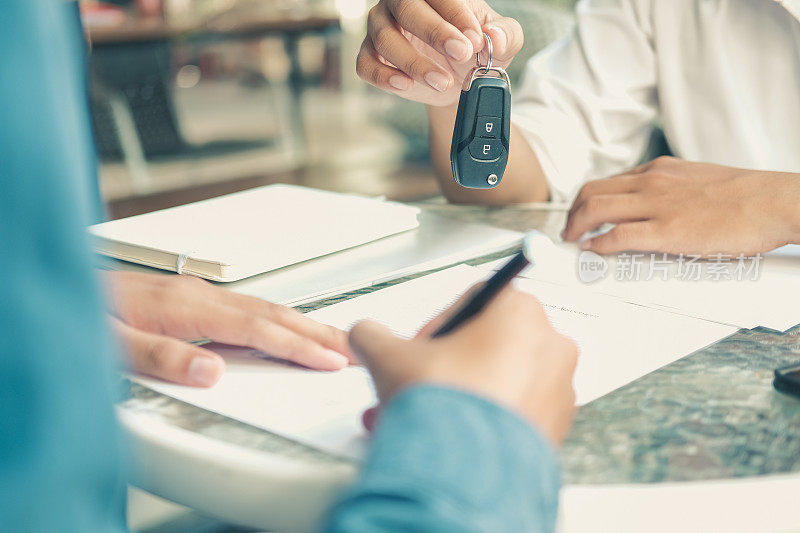 汽车经销商将钥匙交给车主。客户签署保险文件或汽车租赁表格
