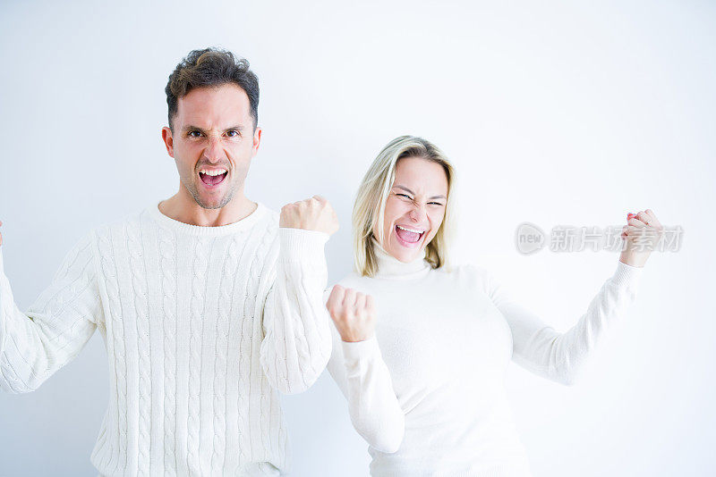 年轻美丽的夫妇穿着休闲t恤站在孤立的白色背景庆祝惊讶和惊讶的成功与双臂举起和睁开眼睛。赢家的概念。