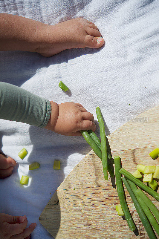 婴儿从一个心形的木砧板上抓豆和去皮的西葫芦