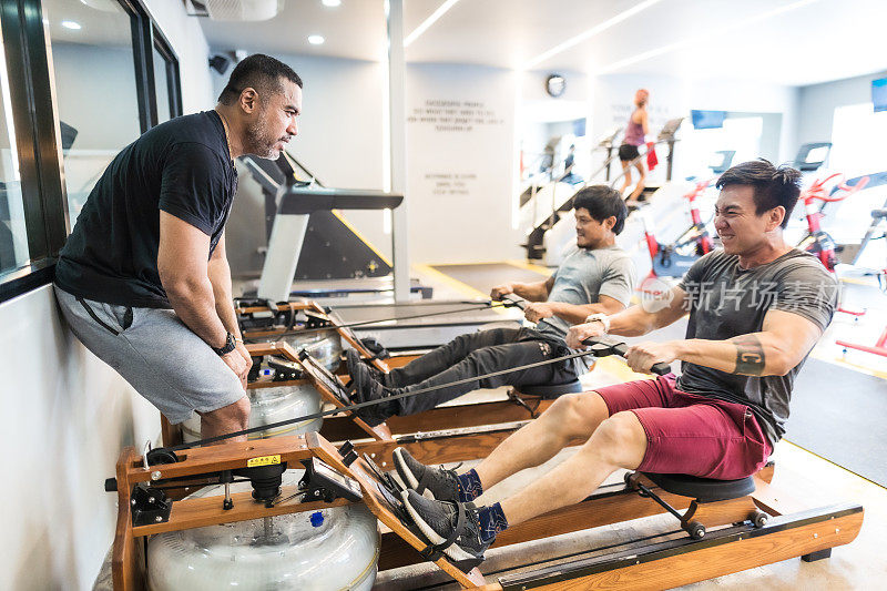 三个亚洲男人在现代健身房使用划船机