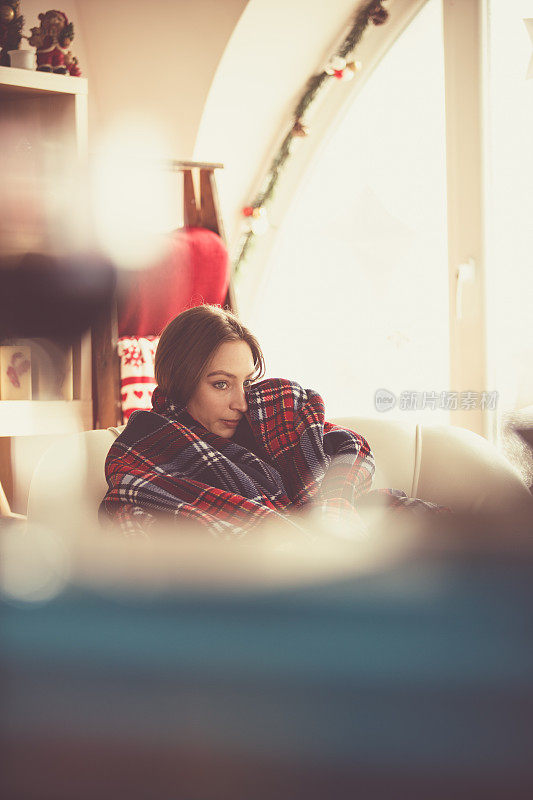 年轻女子裹着一条舒适的毯子在她的客厅里放松