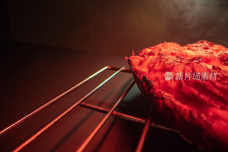 特写微距拍摄的美味热气腾腾的深盘辣香肠披萨新鲜出炉的烤箱在冷却架下的加热灯与复制空间