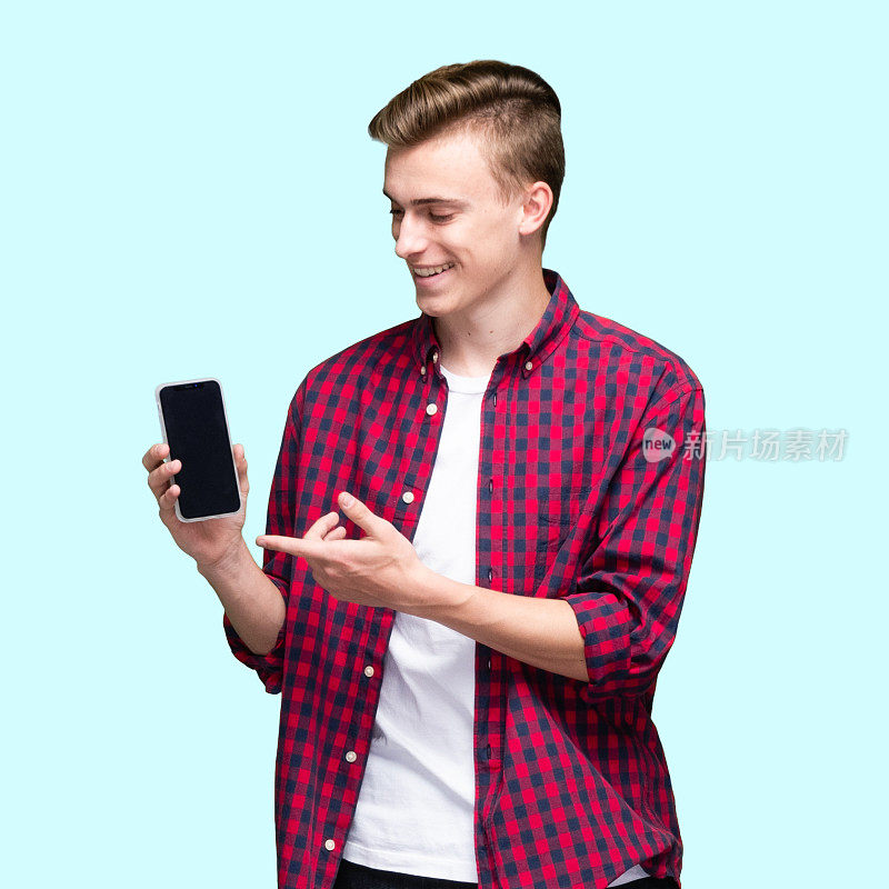 十几岁的男孩穿着衬衫站在蓝色背景前使用智能手机