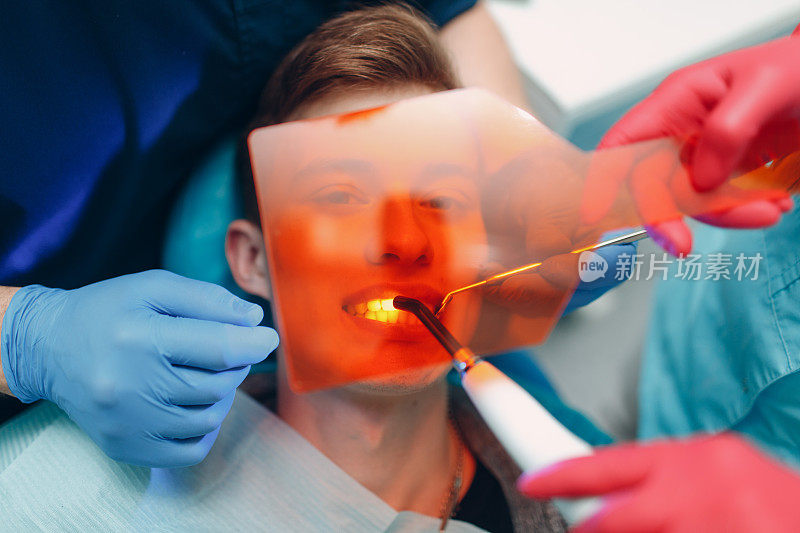牙医。牙医和病人。光固化密封。紫外线牙科灯和橙色保护玻璃。补牙材料。