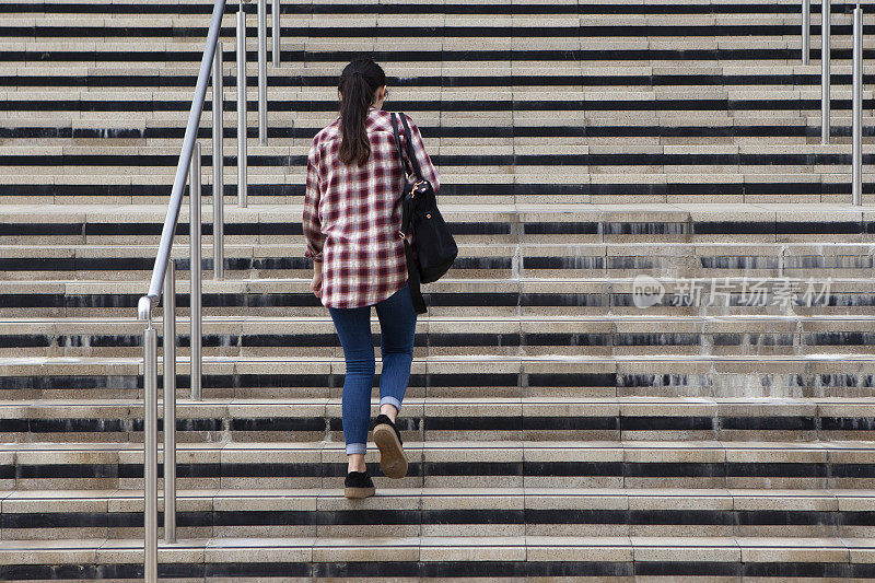 一名女学生走上台阶，进入一所大学大楼，从后面看到有复印空间