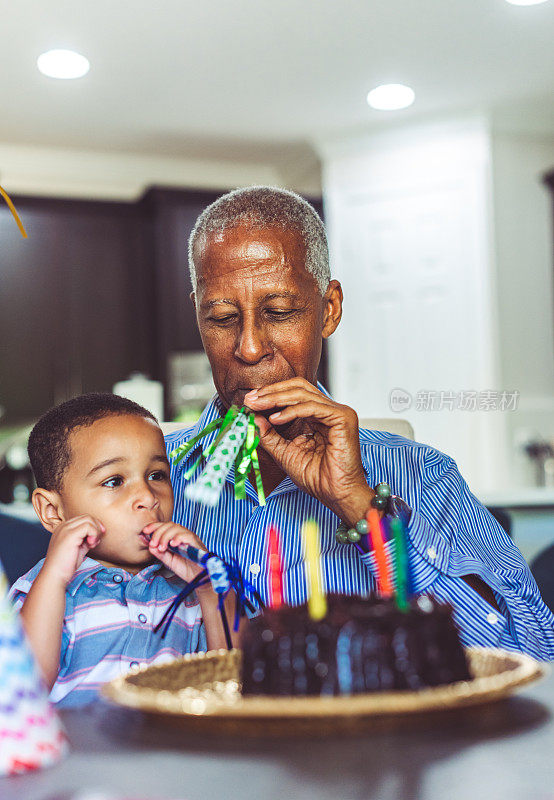 非裔美国人祖父和孙子在家庭生日庆典上吹响派对号角