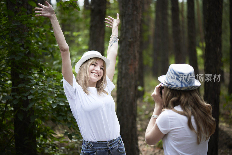 戴着帽子的快乐女人在公园里被她的女朋友拍照。