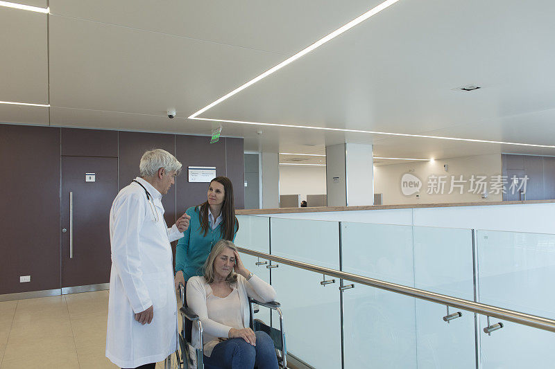 资深医生在夹层走廊与坐轮椅的病人和亲属交谈