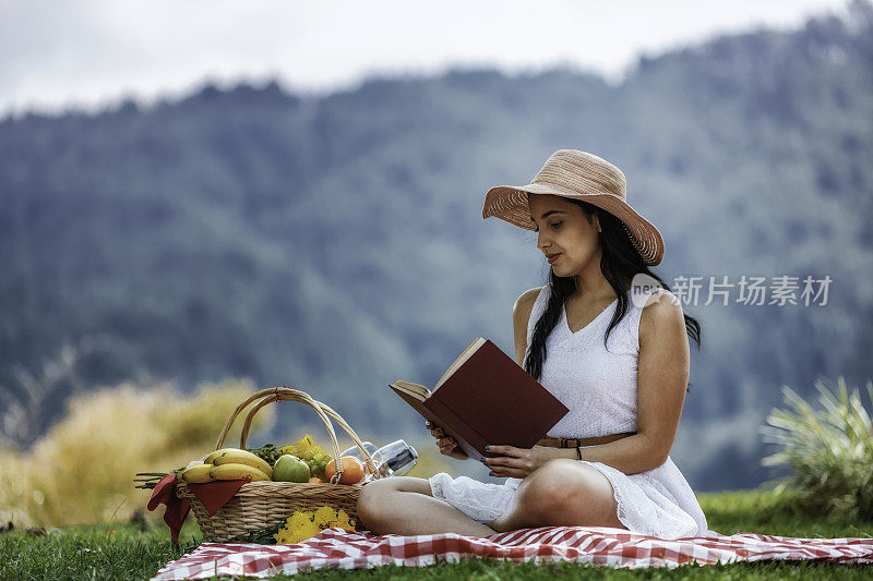 放松可爱的西班牙年轻女子读一本书在草地上。野餐和日间户外休闲活动。