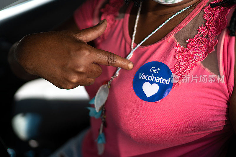 坐在车里的女人指着一个贴着“接种疫苗”标签的口罩