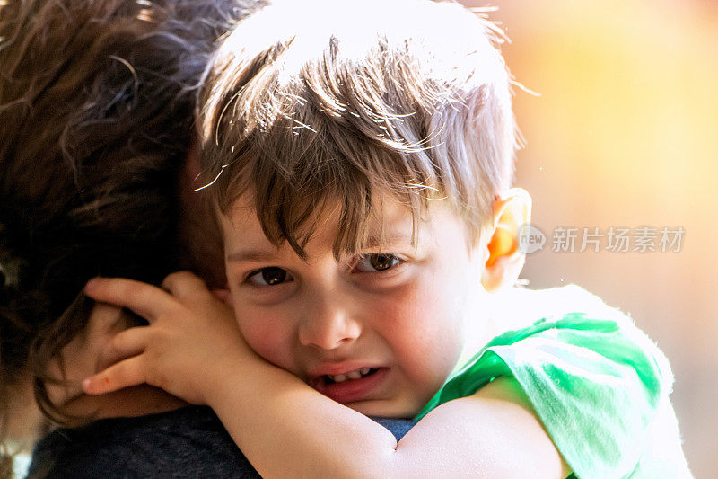一个哭泣的小男孩拥抱着他的母亲，看着镜头