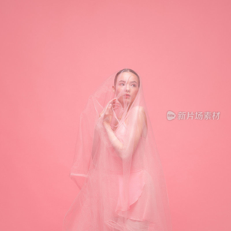 一个年轻美丽优雅的芭蕾舞者跳舞与白色面纱摆姿势孤立在粉红色的工作室背景。艺术，运动，动作，灵活性，灵感概念。