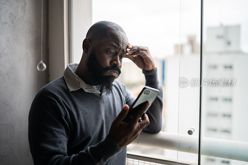 中年男子在窗边用智能手机看坏消息
