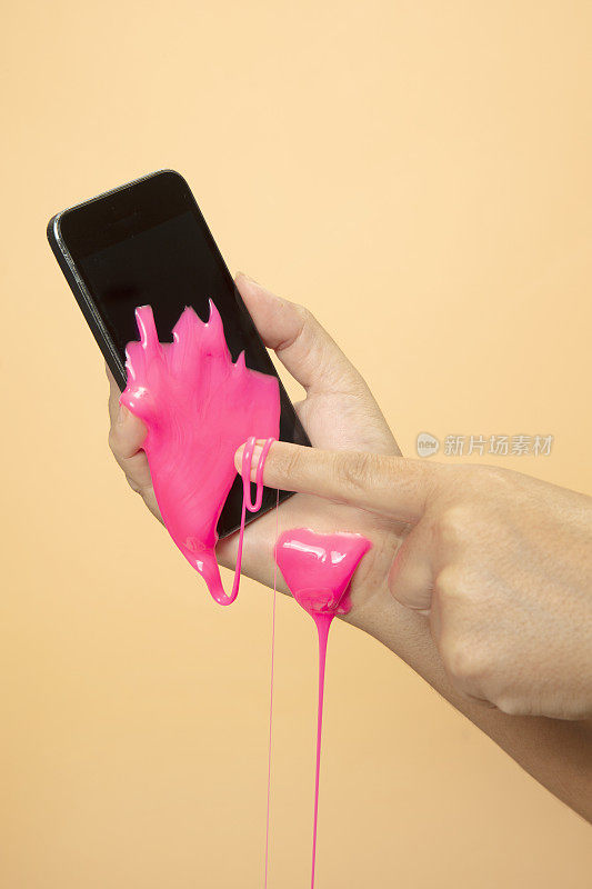 女人的手使用智能手机与霓虹灯粉色黏液玩具在橙色流行艺术背景。