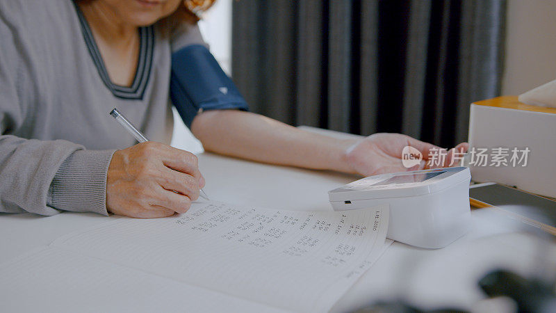 老年妇女在家里的笔记本上手工检查血压，记录她的血压数字。