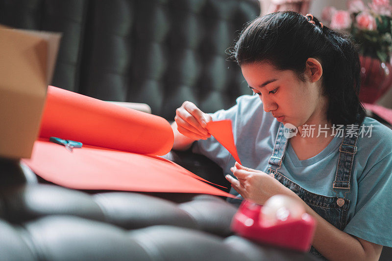 亚洲年轻的十几岁的女孩制作手工物品照顾包剪纸红纸准备发送给她的家人或朋友从远方。