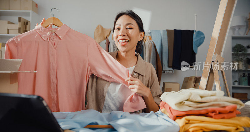 亚洲女商人直播电子商务在家里卖衣服，美丽的女孩使用智能手机和平板电脑录制视频。