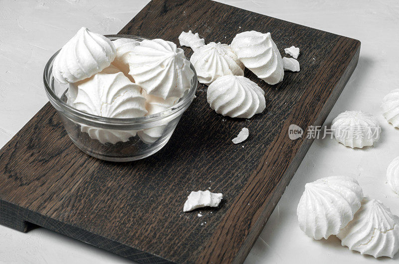 法式蛋白糖霜甜点放在灰色背景的深色木板上的玻璃碗里。到处都是完整的和破碎的蛋白酥皮。侧视图。