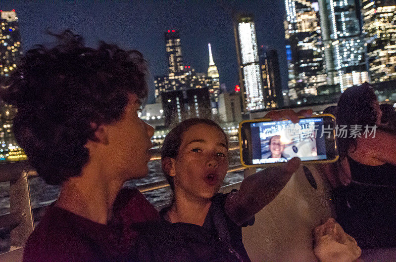 十几岁的女孩显示自拍与纽约摩天大楼在晚上