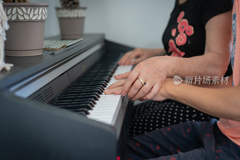 特写老年妇女教一个小男孩用乐谱弹钢琴。