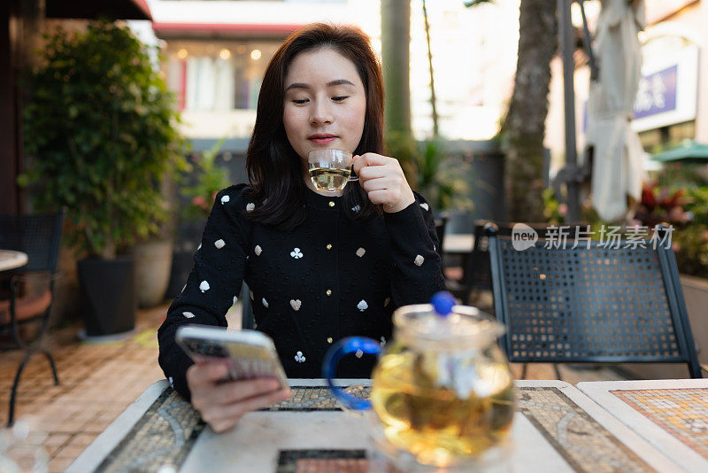 亚洲女孩边喝茶边用智能手机