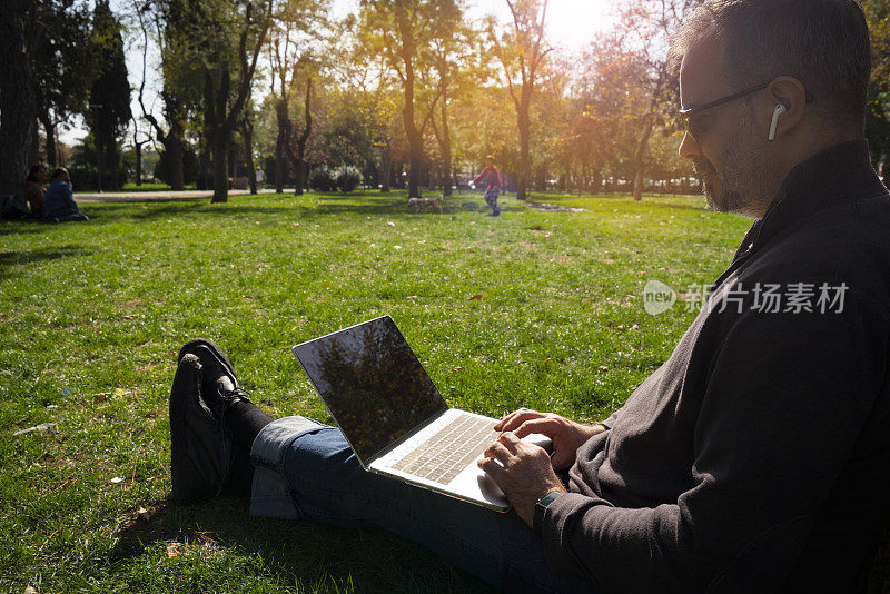自由职业者坐在公园里，拿着笔记本电脑，喝着咖啡