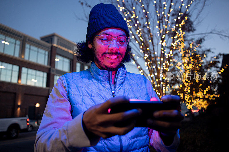 高大年轻的非洲裔男子水平拿着智能手机在市中心玩电子游戏