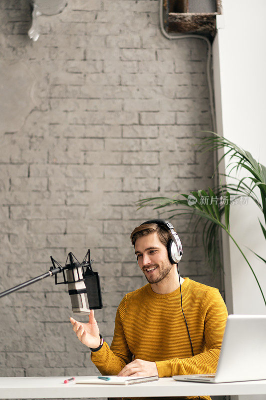 男子博主微笑着在演播室用耳机、笔记本电脑和耳机直播他的音频播客