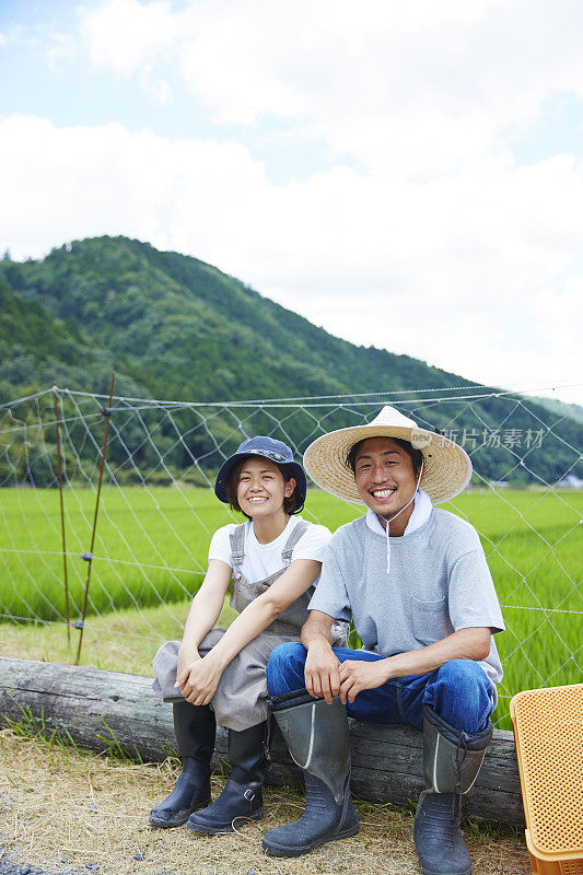 微笑的男男女女坐在稻田前的圆木上