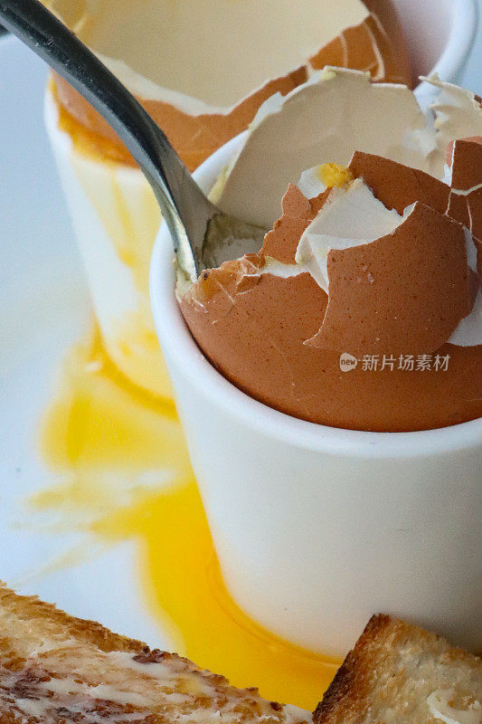 全画幅黄油吐司士兵与两个空蛋壳鸡蛋杯在白盘子，吃软煮鸡蛋与溏心黄色蛋黄，金属茶匙，重点在前景