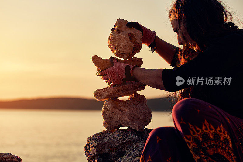 一个女人的剪影平衡岩石和石头上的海洋海岸在日落日出的时候。