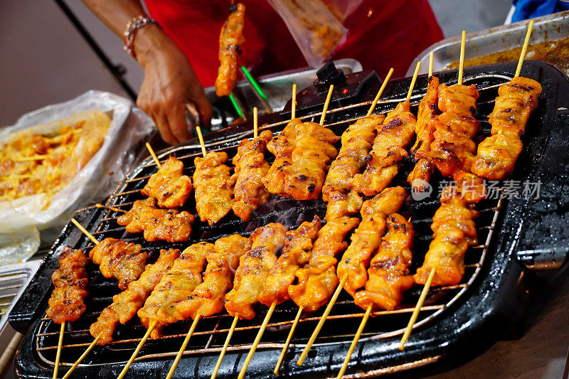用竹签在电炉上烤鸡，卖家的手在烤架上烤鸡。烤鸡烧烤特写。美味的亚洲料理。马来西亚沙爹鸡。