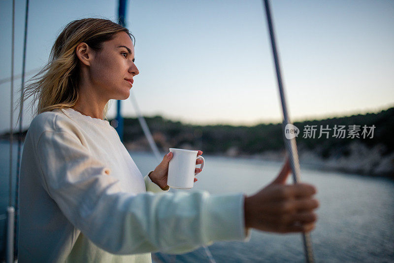 在一个寒冷的秋日，一个淡季的假期，美丽的女人在帆船甲板上享受早晨的咖啡